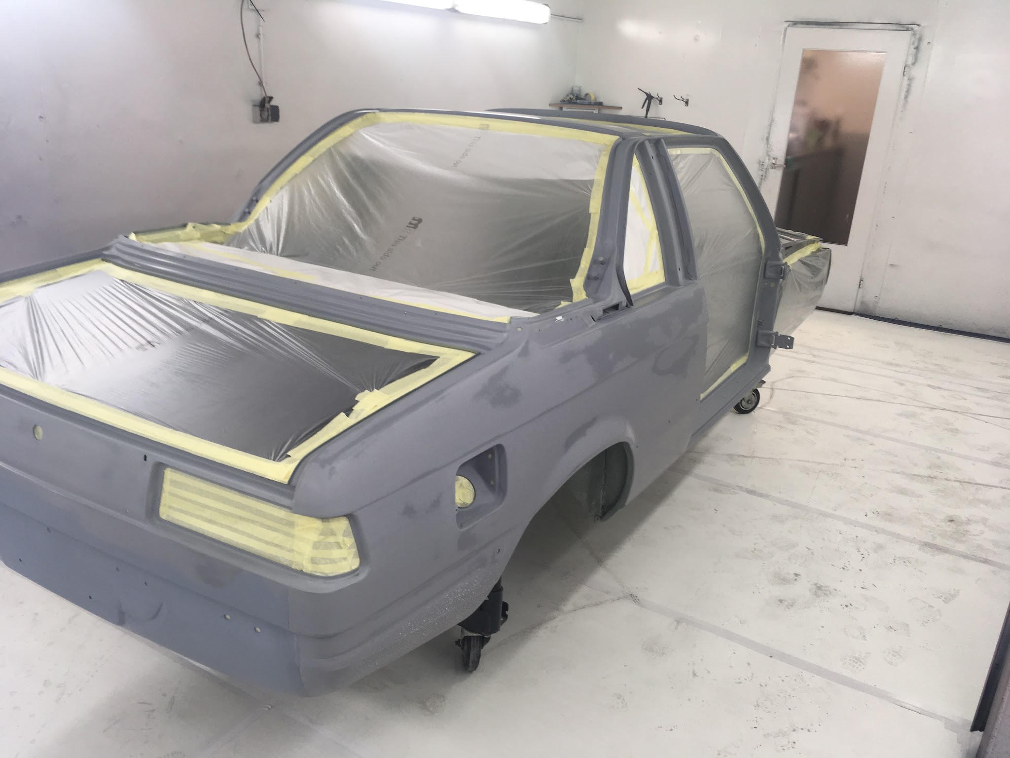 Carrosserie in grondlak in de spuitcabine, afgeplakt met tape en folie