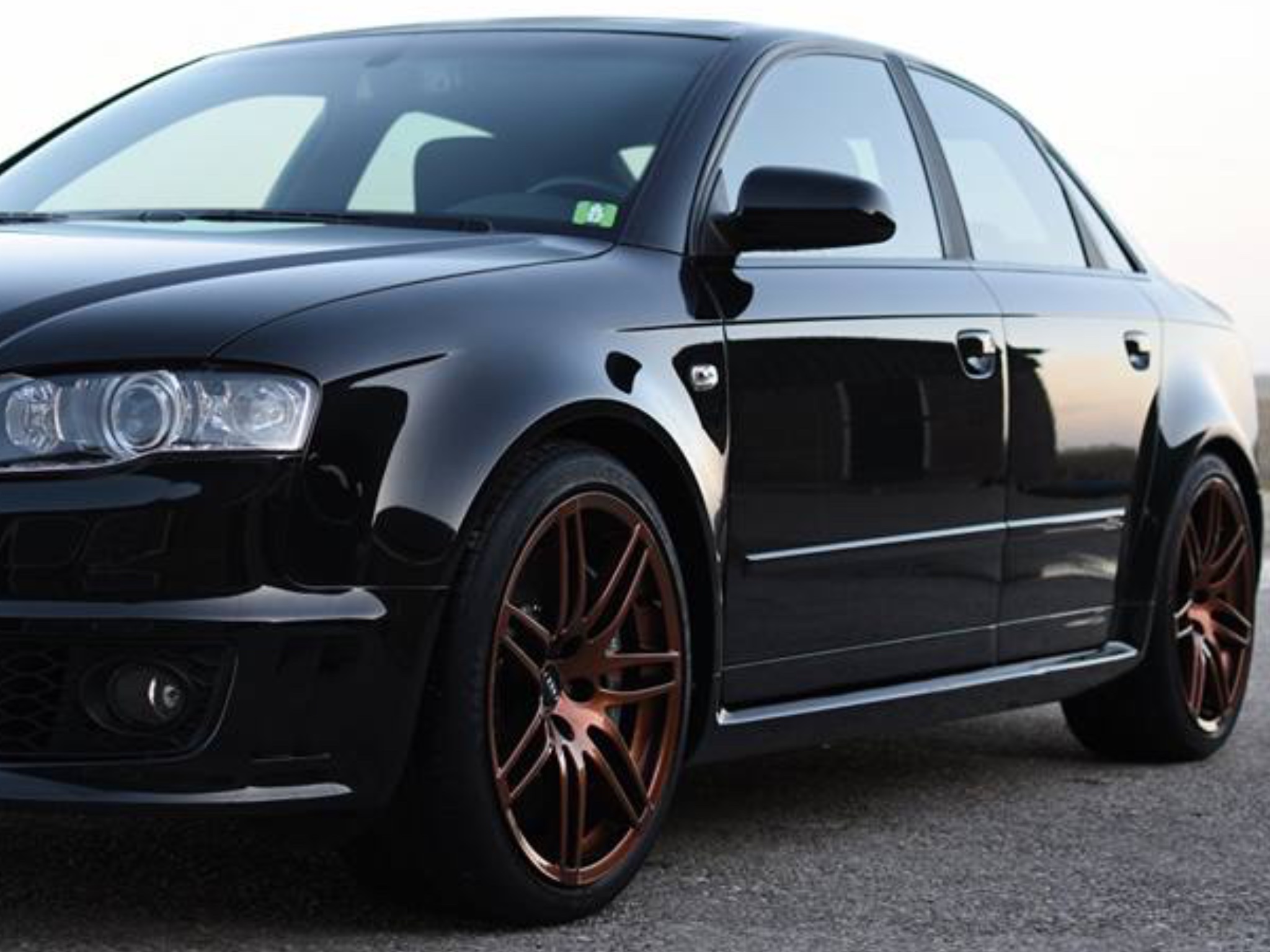 Zwarte Audi A4 met bronskleurige velgen, buiten bij avondlicht