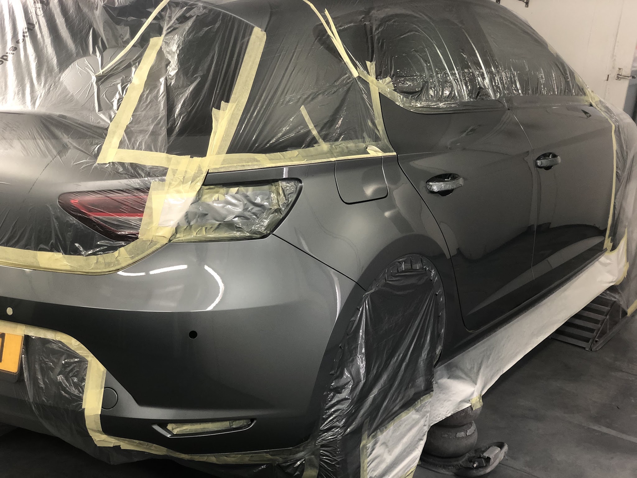 Donkergrijze hatchback, achterzijde afgeplakt voor het spuiten